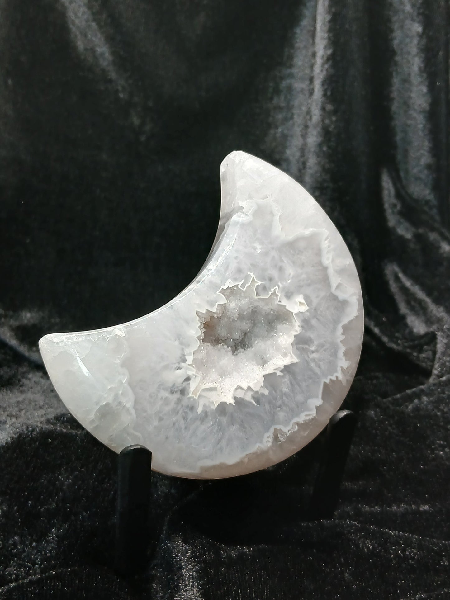 Fordite Haus: Crystals & Fordite agate moon carving with a central druzy geode cavity on a black display stand