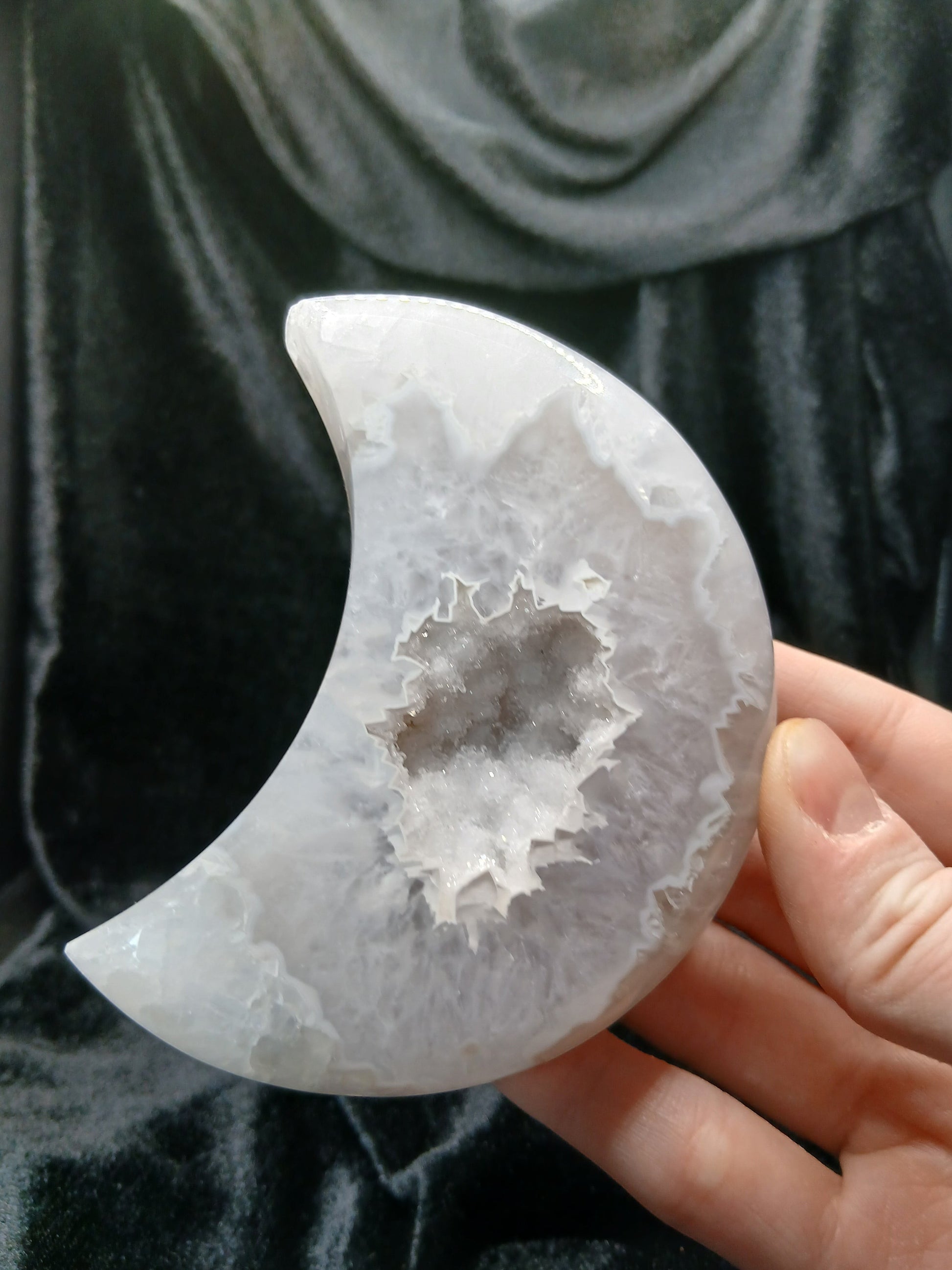 Fordite Haus: Crystals & Fordite agate moon carving with a central druzy geode cavity held in a hand.
