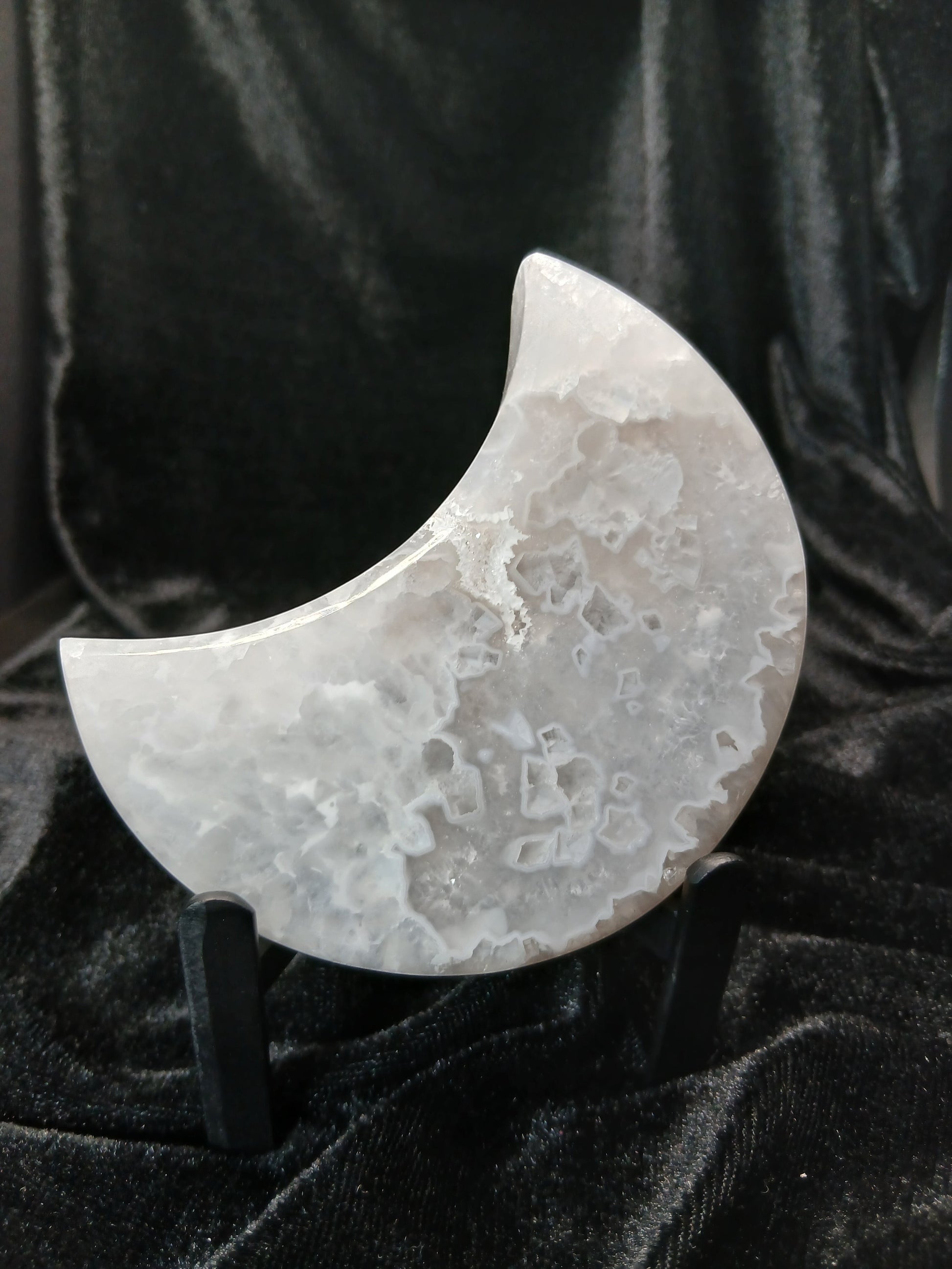 Fordite Haus: Crystals & Fordite agate moon carving with sparkling druzy texture on a black display stand