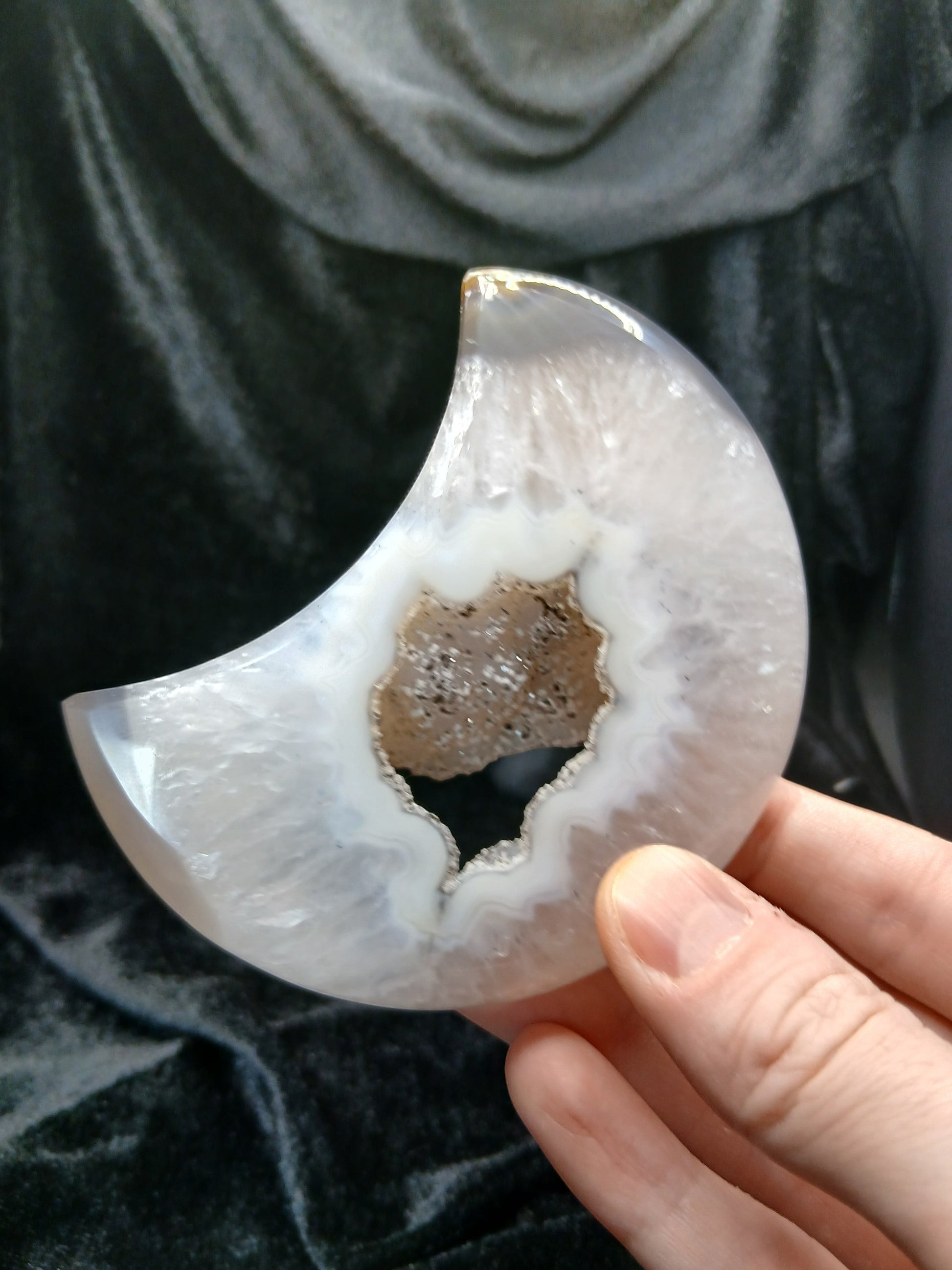 Fordite Haus: Crystals & Fordite agate moon carving with a central druzy geode cavity held in a hand.