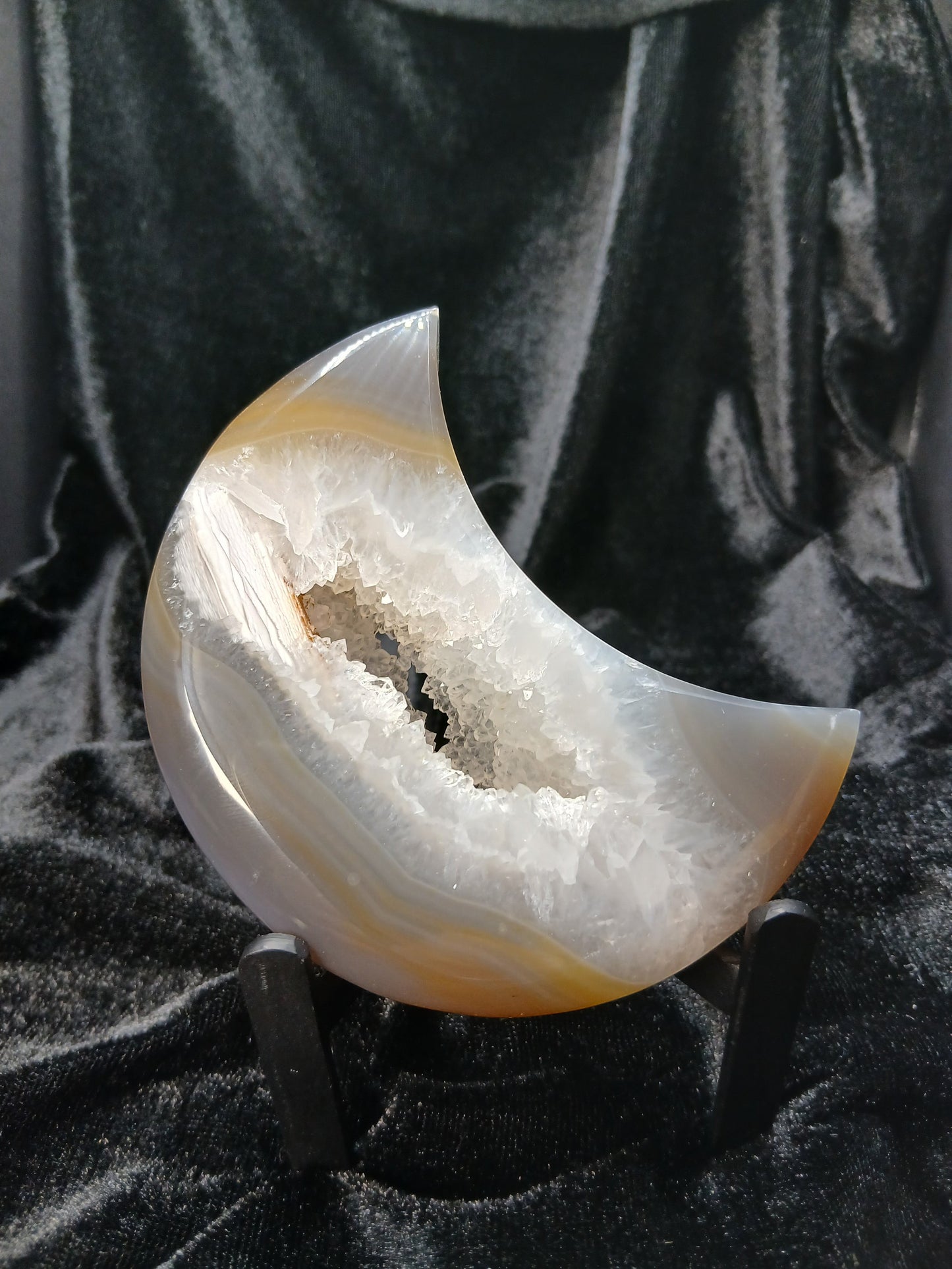 Fordite Haus: Crystals & Fordite agate moon carving with a central druzy geode cavity on a black display stand.