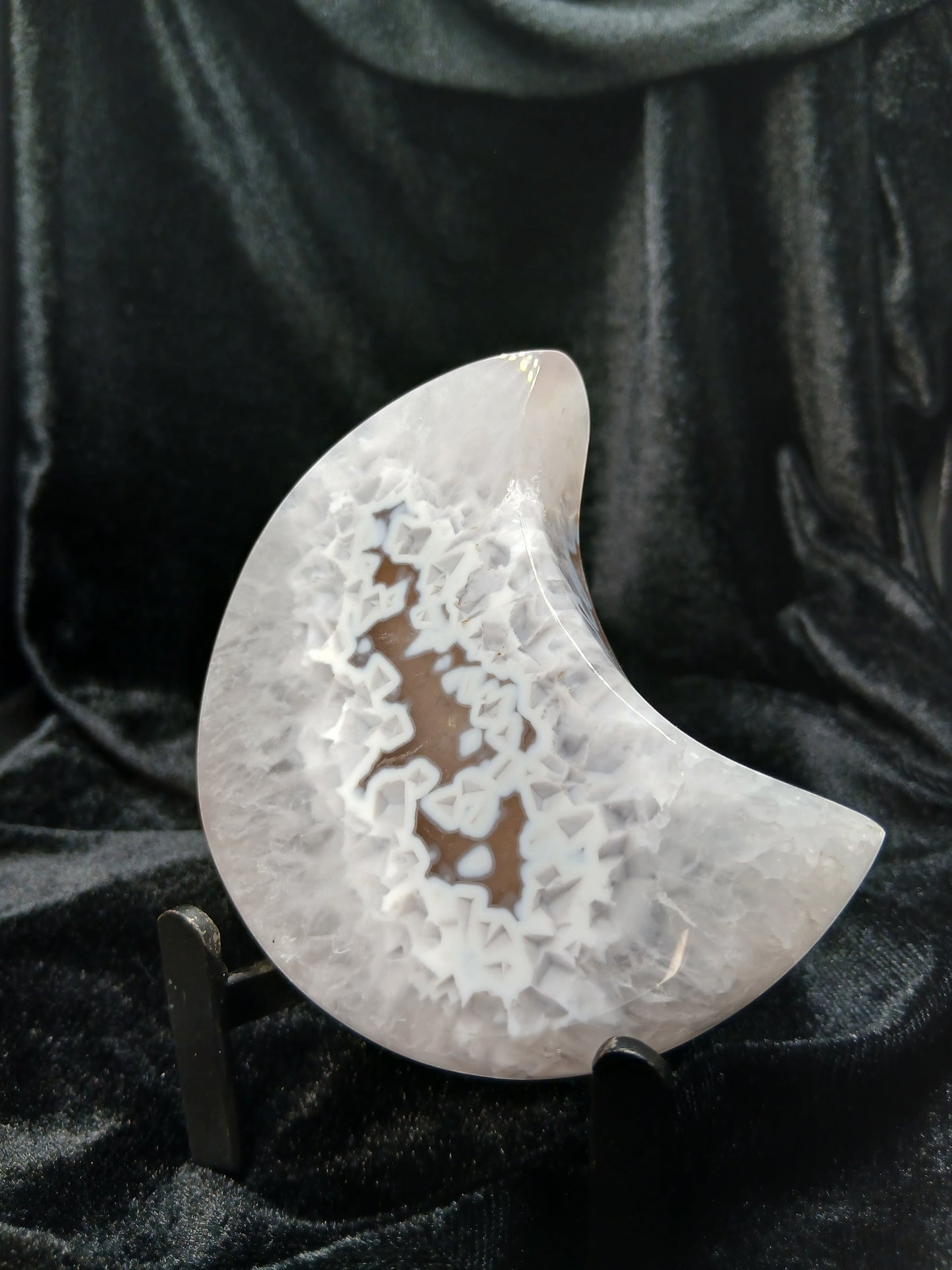 Fordite Haus: Crystals & Fordite agate moon carving with intricate white crystalline patterns on a black stand.