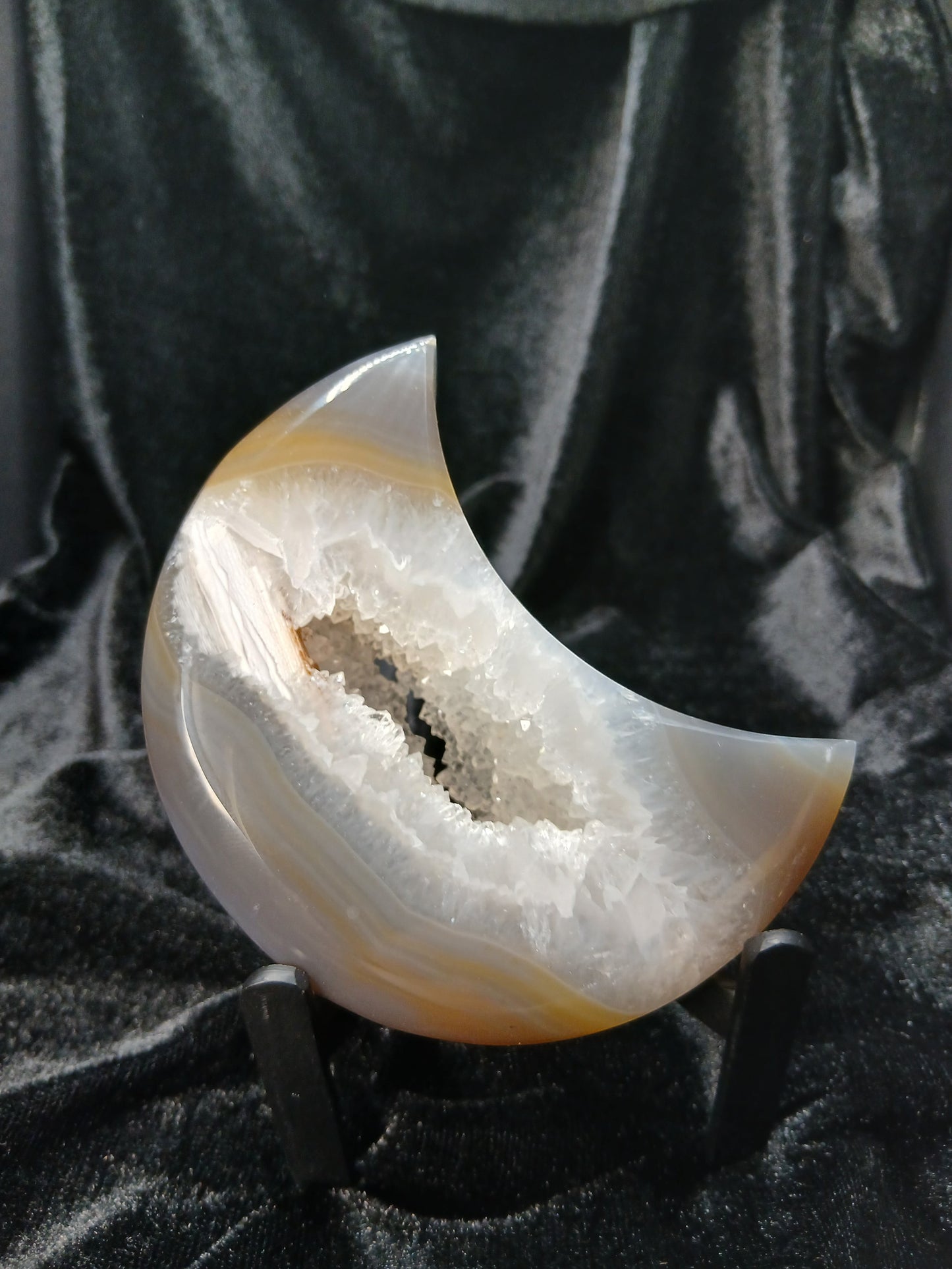 Fordite Haus: Crystals & Fordite agate moon carving with a sparkling crystal geode center on a black display stand.
