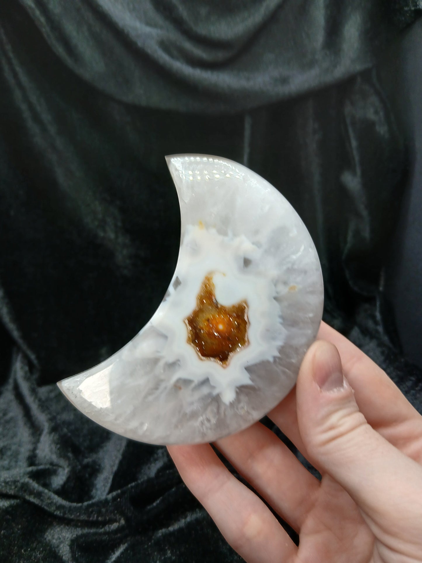 Fordite Haus: Crystals & Fordite agate moon carving with a central amber geode pocket held in hand.