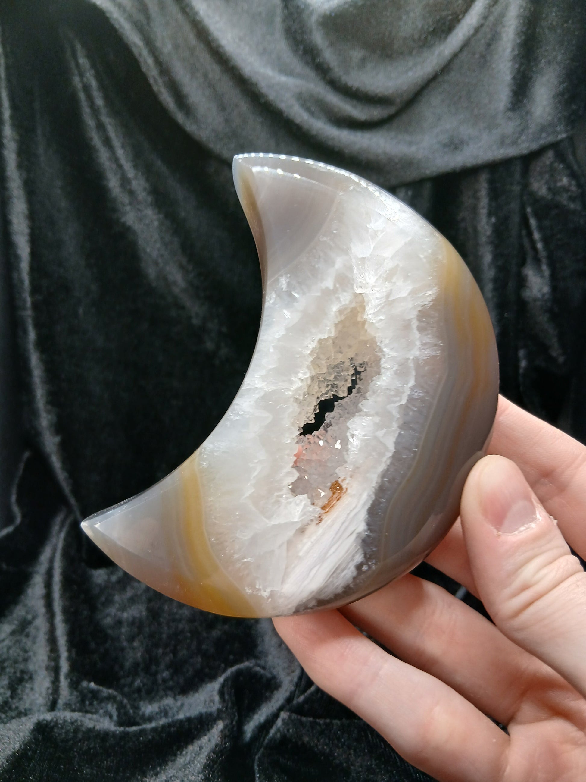 Fordite Haus: Crystals & Fordite agate moon carving with a central druzy geode cavity held in a hand.
