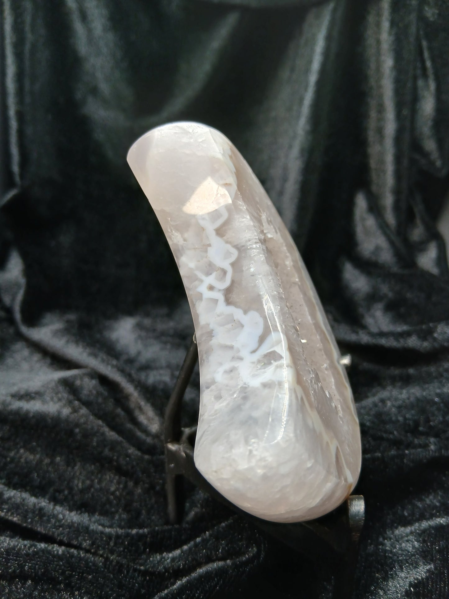 Fordite Haus: Crystals & Fordite agate moon carving with white crystalline patterns on a black velvet display stand.
