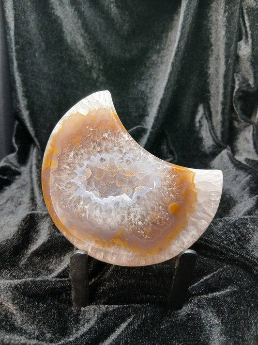Fordite Haus: Crystals & Fordite agate moon carving with crystalline geode center on a black display stand.