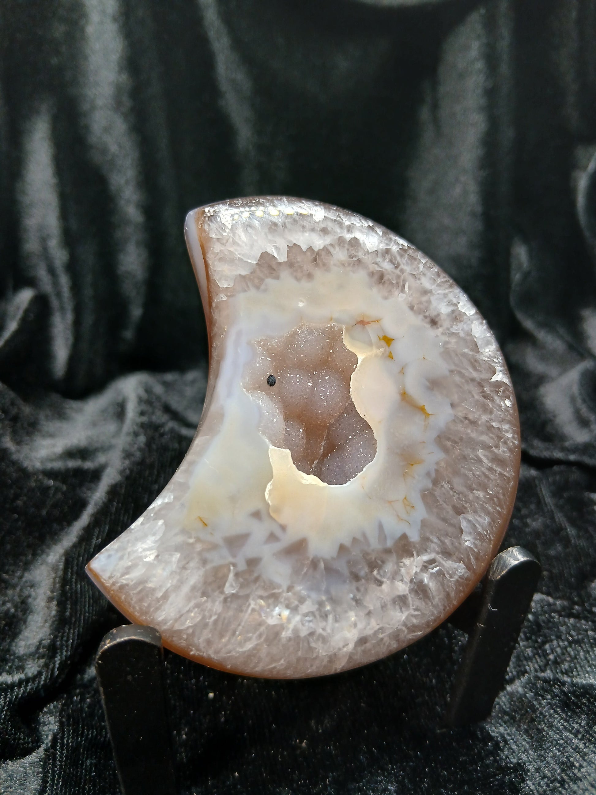 Fordite Haus: Crystals & Fordite taupe and white agate moon carving with a central druzy geode on a display stand.