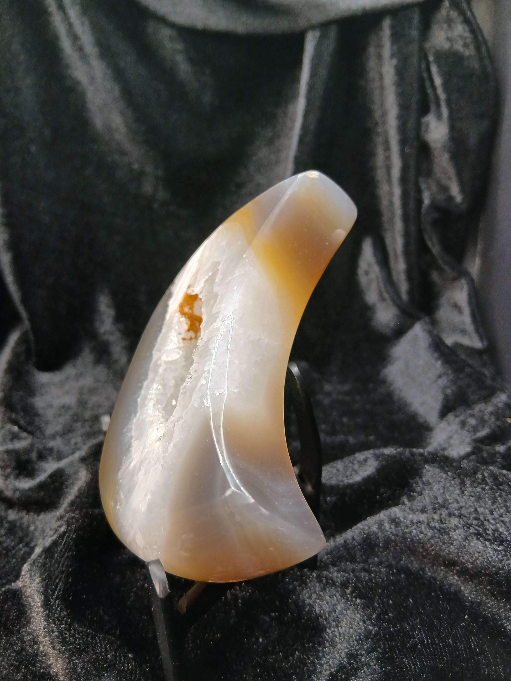 Fordite Haus: Crystals & Fordite agate moon carving with a central druzy geode cavity on a black display stand.
