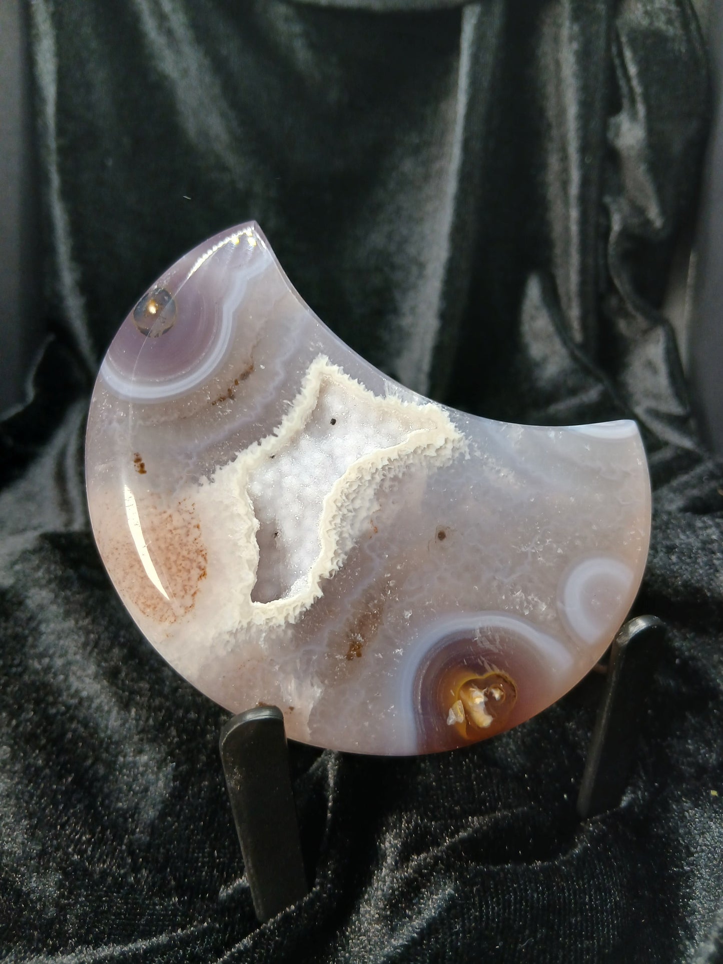 Fordite Haus: Crystals & Fordite agate moon carving with a central druzy geode pocket on a black display stand.