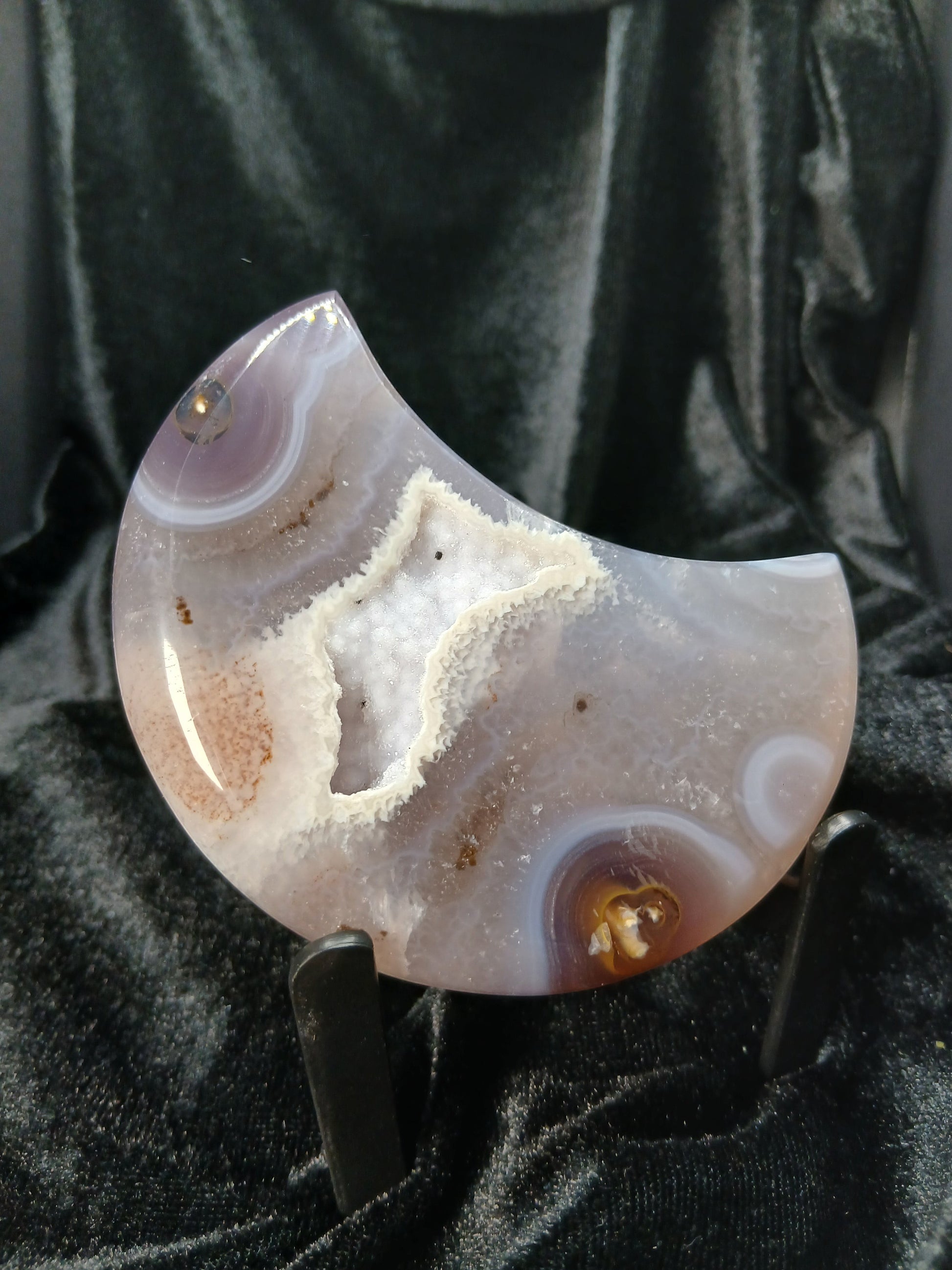 Fordite Haus: Crystals & Fordite agate moon carving with a central druzy geode pocket on a black display stand.