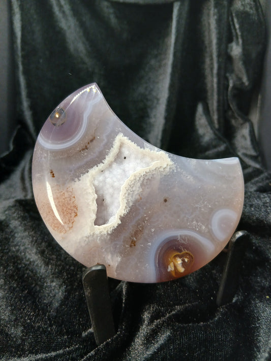 Fordite Haus: Crystals & Fordite agate moon carving with a central druzy geode pocket on a black display stand.