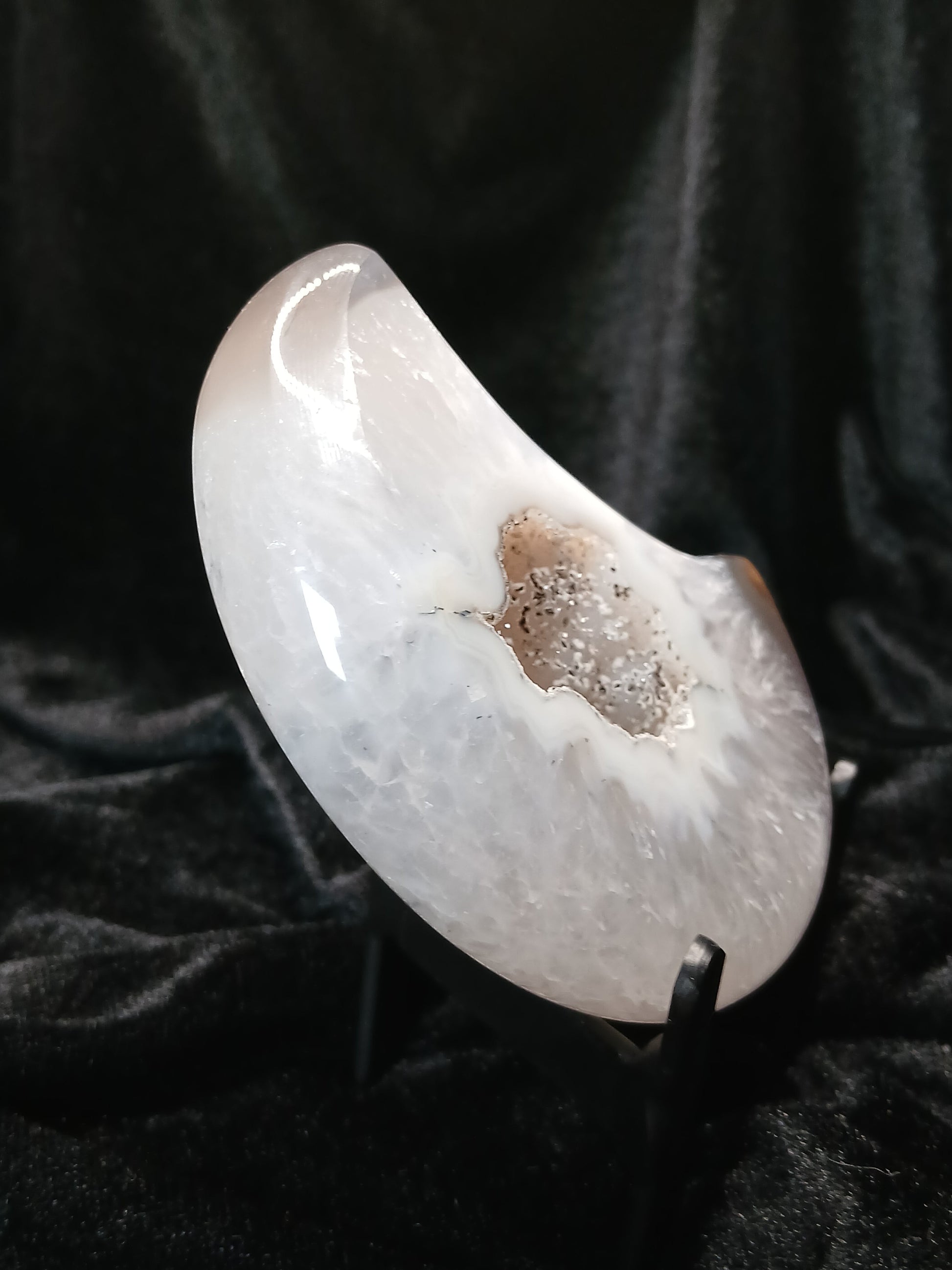 Fordite Haus: Crystals & Fordite white agate moon carving with a central druzy geode pocket on a black display stand