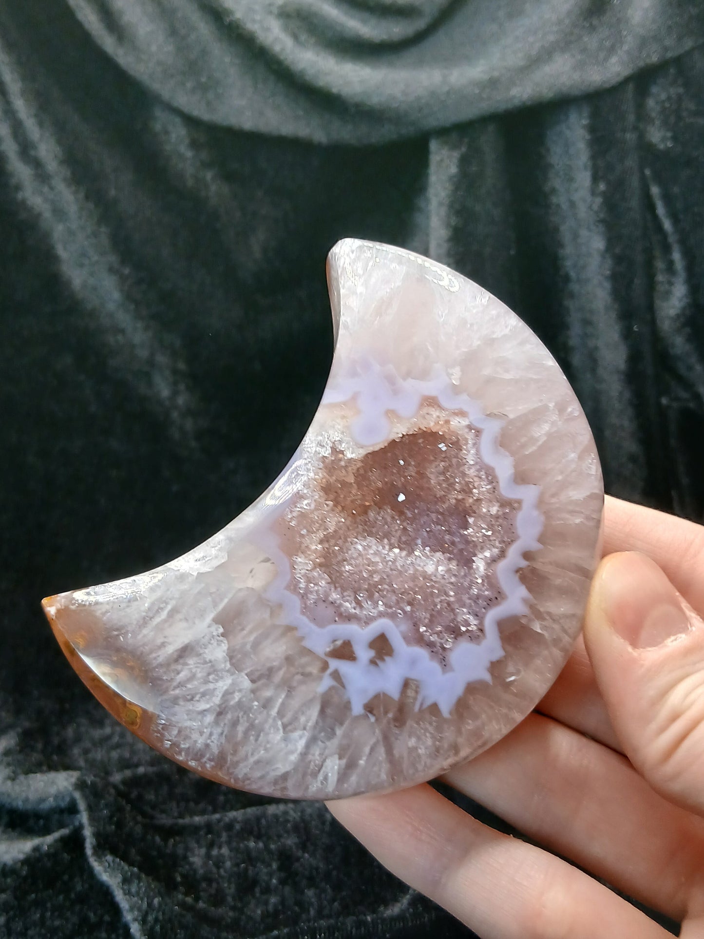 Fordite Haus: Crystals & Fordite agate moon carving with a central sparkling druzy geode held in a hand.