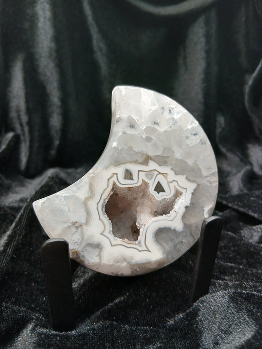 Fordite Haus: Crystals & Fordite 3-inch agate moon carving with a central druzy geode cavity on a black display stand.