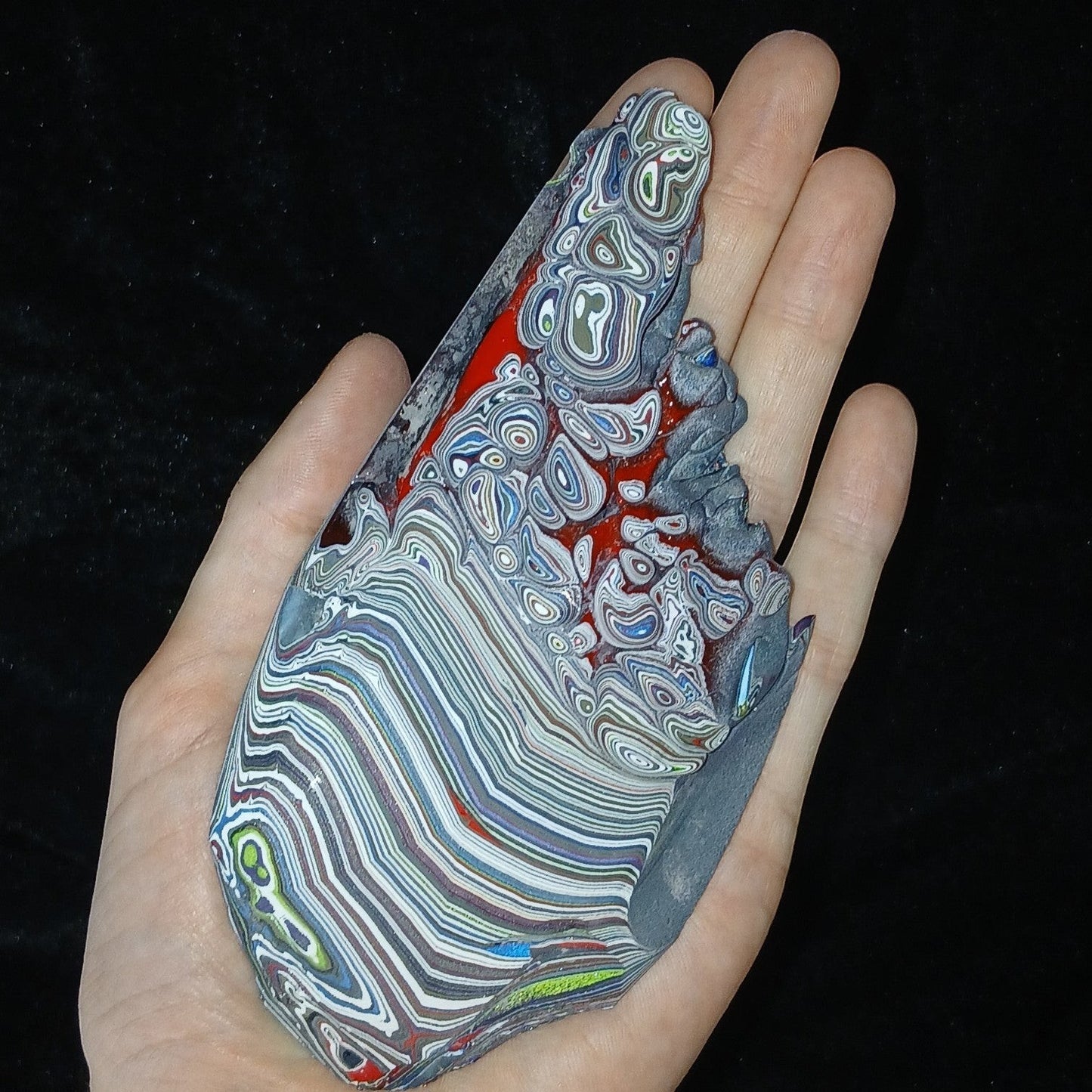 Fordite Haus: Crystals & Fordite 84g Jeepite slab with colorful layered automotive paint swirls held in a hand.