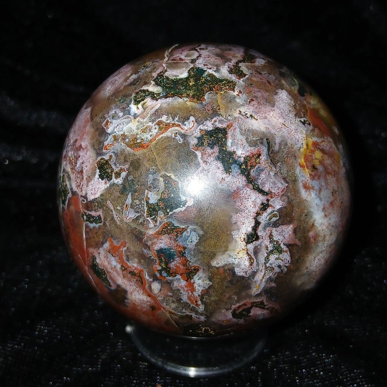 Fordite Haus: Crystals & Fordite 57.3mm Ocean Jasper sphere with greenish-blue, red, pink, and white patterns.