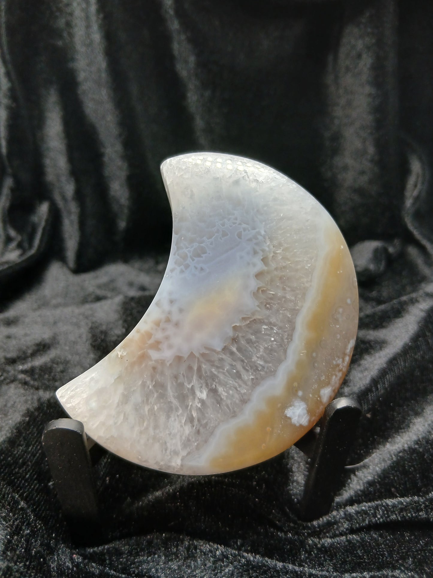 Fordite Haus: Crystals & Fordite crescent moon carving made of peach and cream agate with natural banding on a stand.