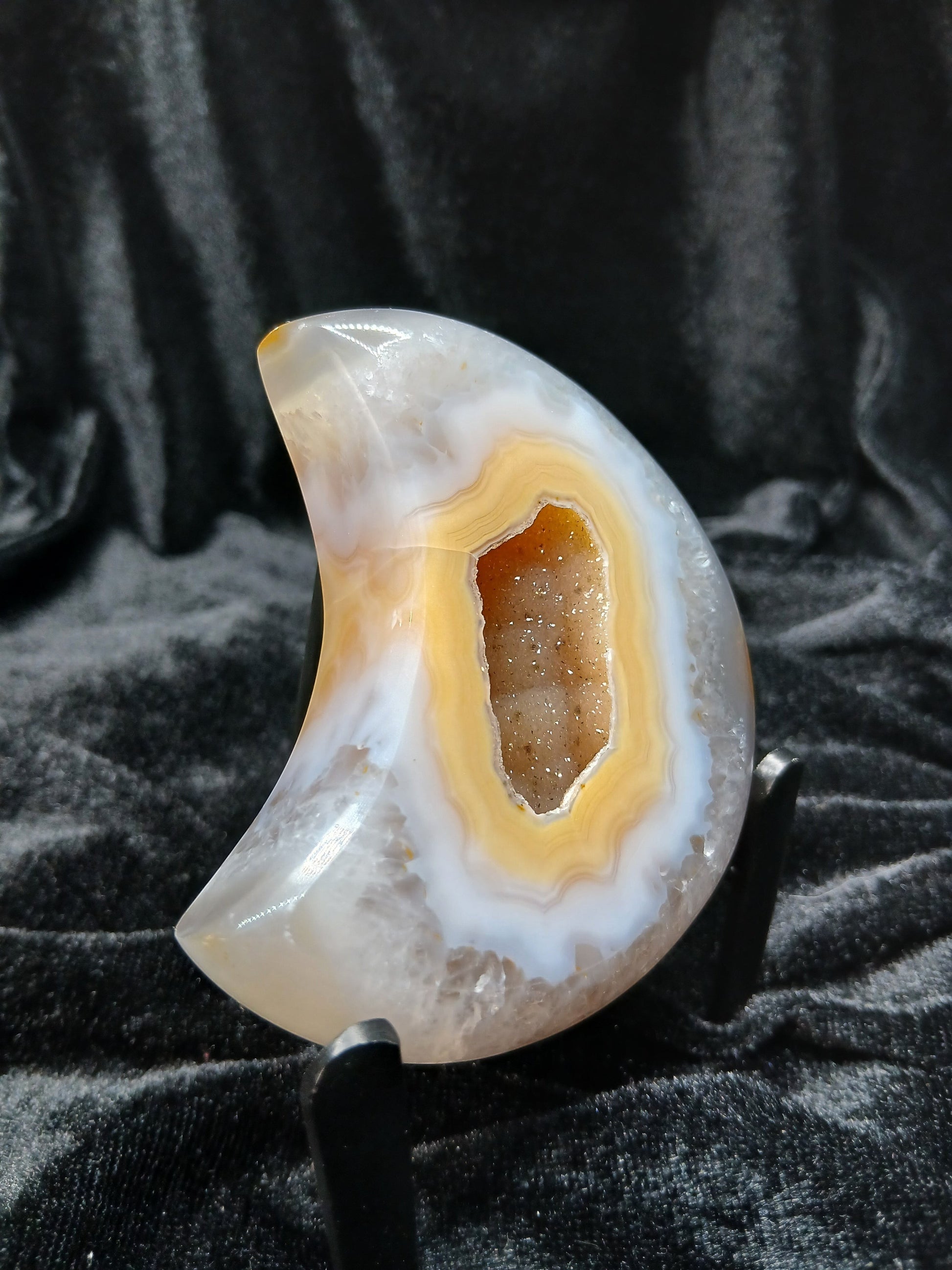 Fordite Haus: Crystals & Fordite peachy agate crescent moon carving with a central druzy geode on a display stand.
