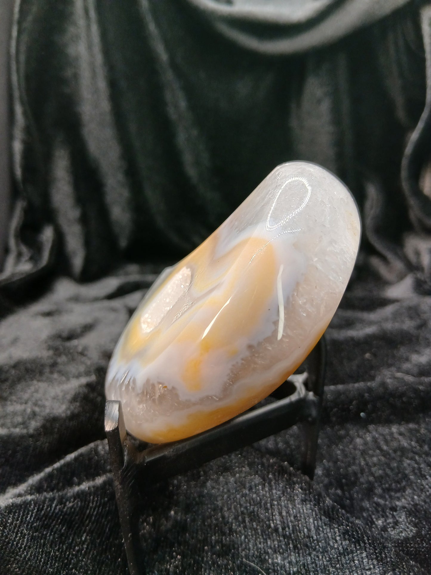 Fordite Haus: Crystals & Fordite peachy agate moon carving with cream banding and translucent edges on a black stand.