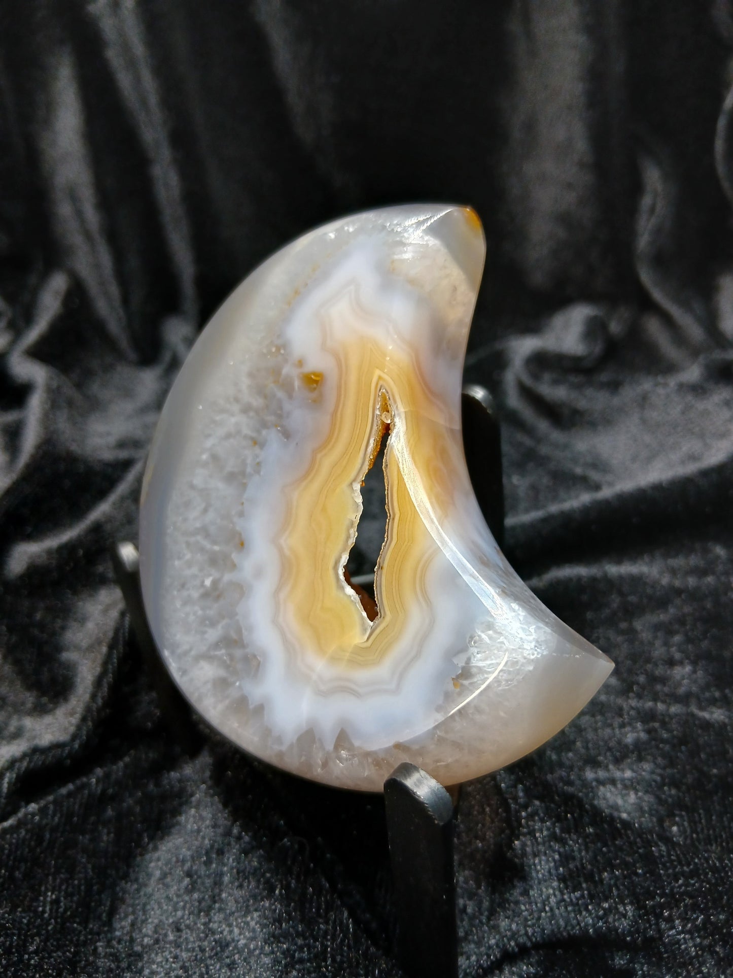 Fordite Haus: Crystals & Fordite peachy agate crescent moon carving with natural banding on a black display stand.
