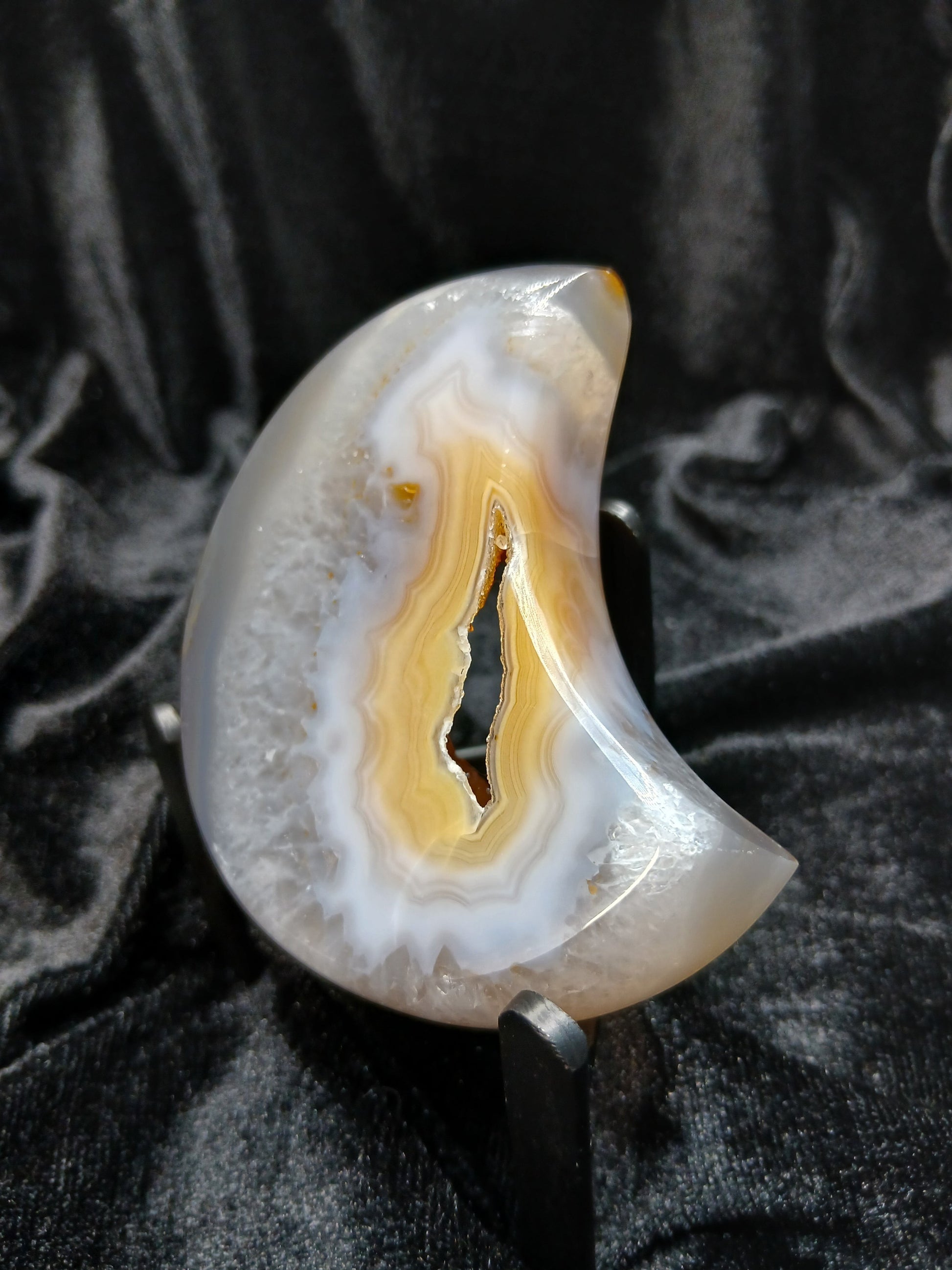 Fordite Haus: Crystals & Fordite peachy agate crescent moon carving with natural banding on a black display stand.