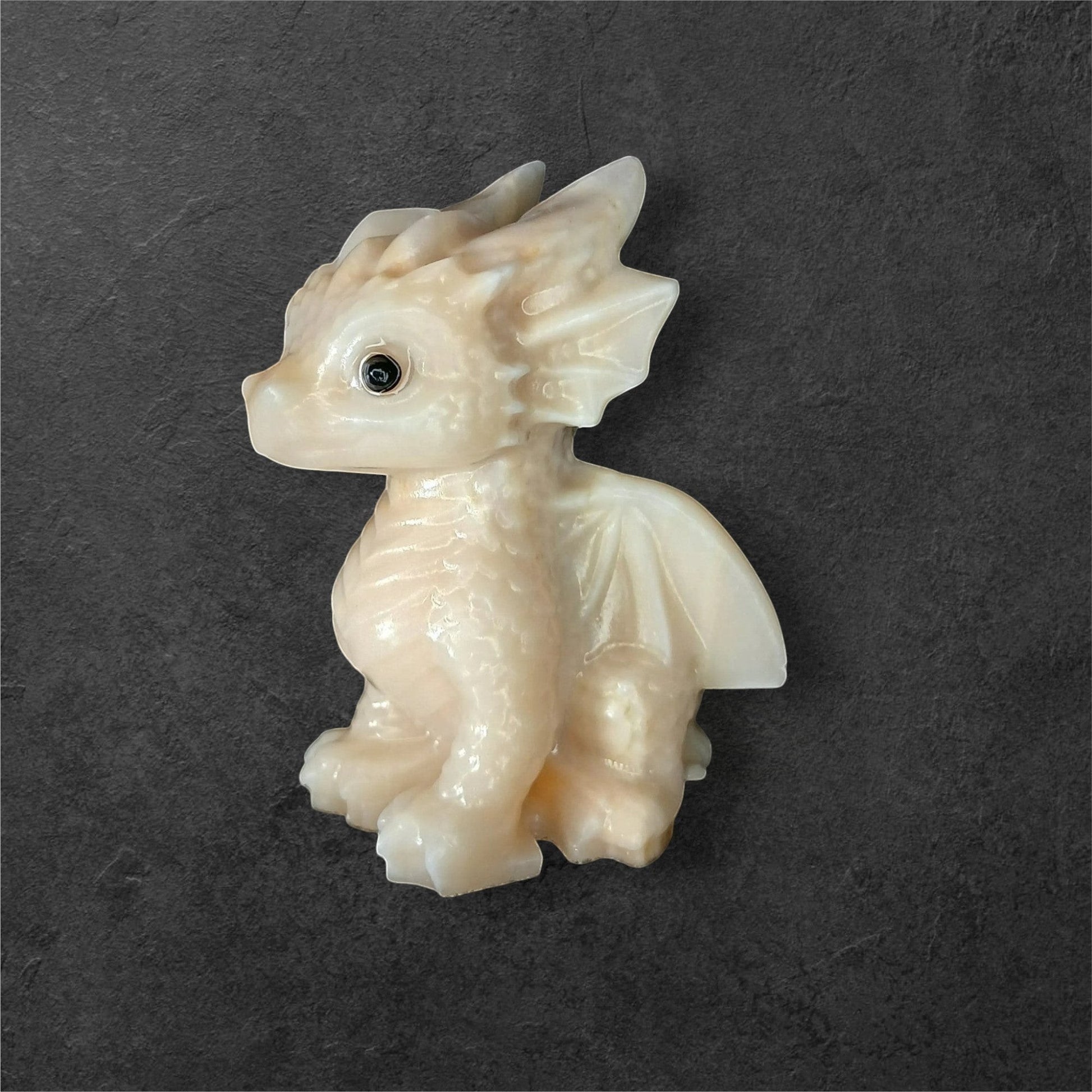 Fordite Haus: Crystals & Fordite light yellow calcite dragon figurine with smooth, carved details on a dark background.