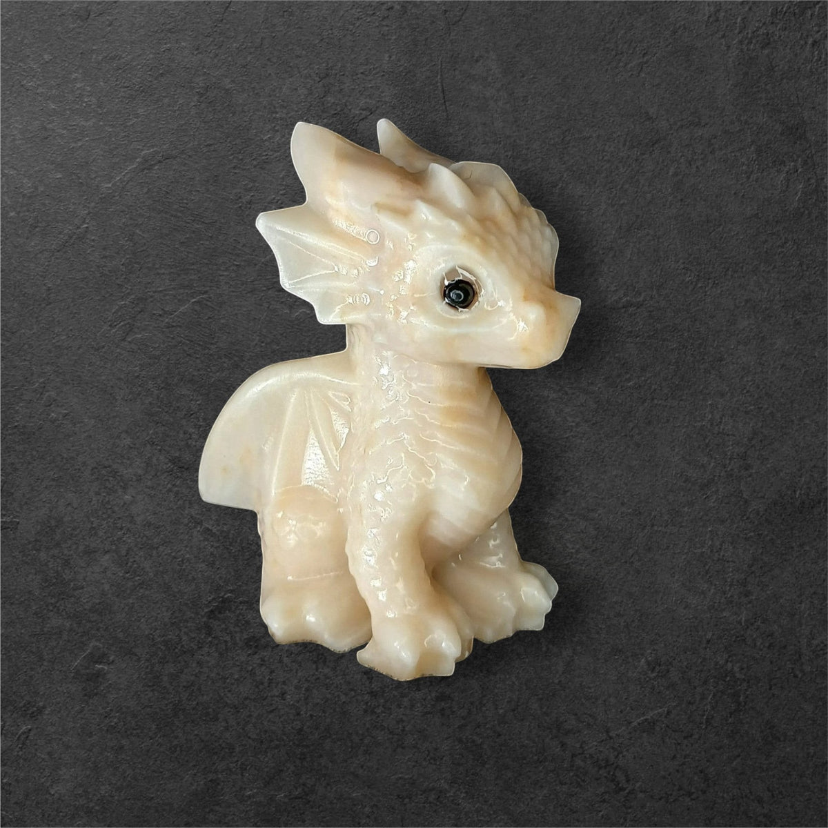 Fordite Haus: Crystals & Fordite light yellow calcite dragon figurine with smooth texture on a dark background.